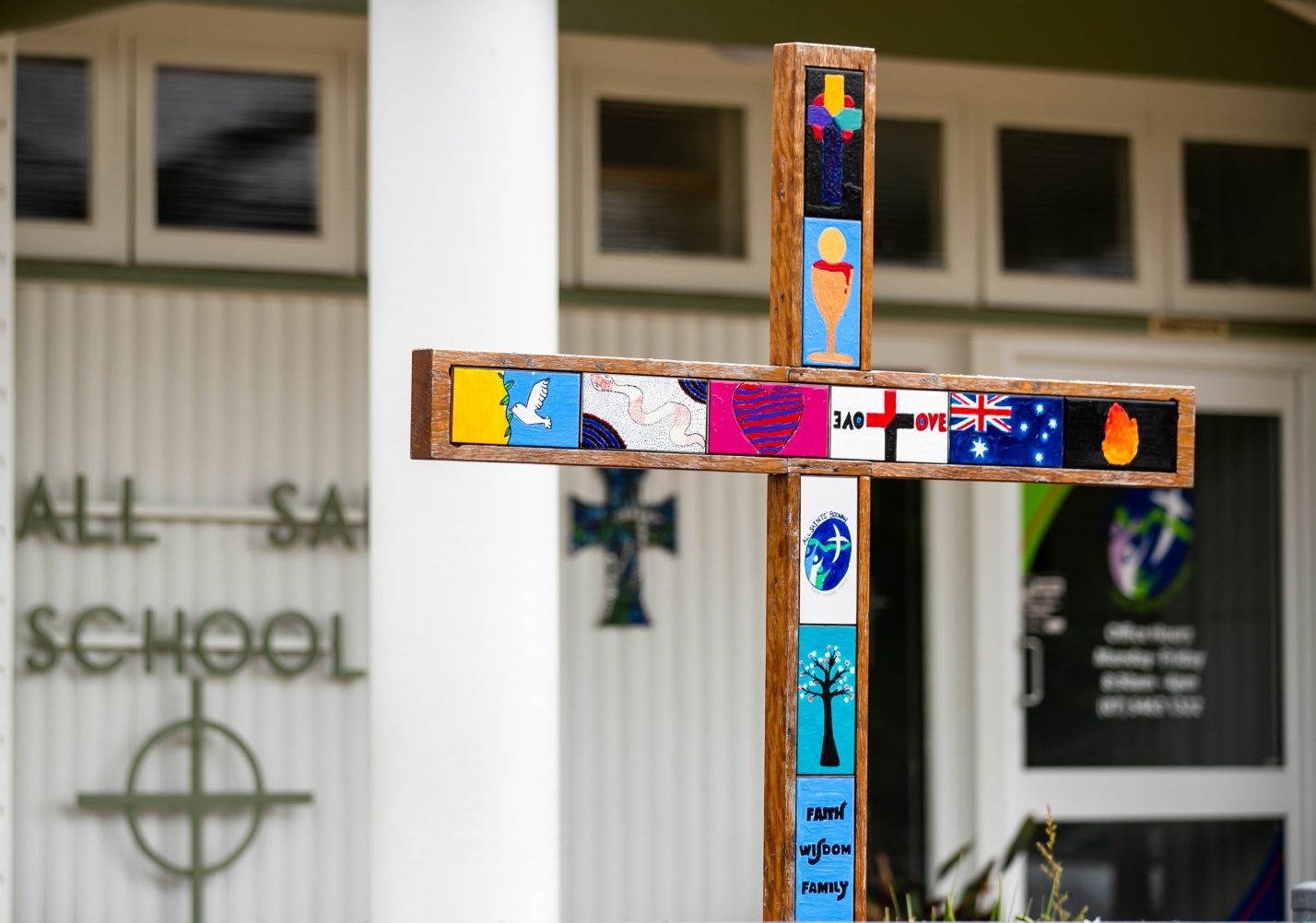 Wooden cross decorated with colourful student artwork and religious symbols displayed outside a school building