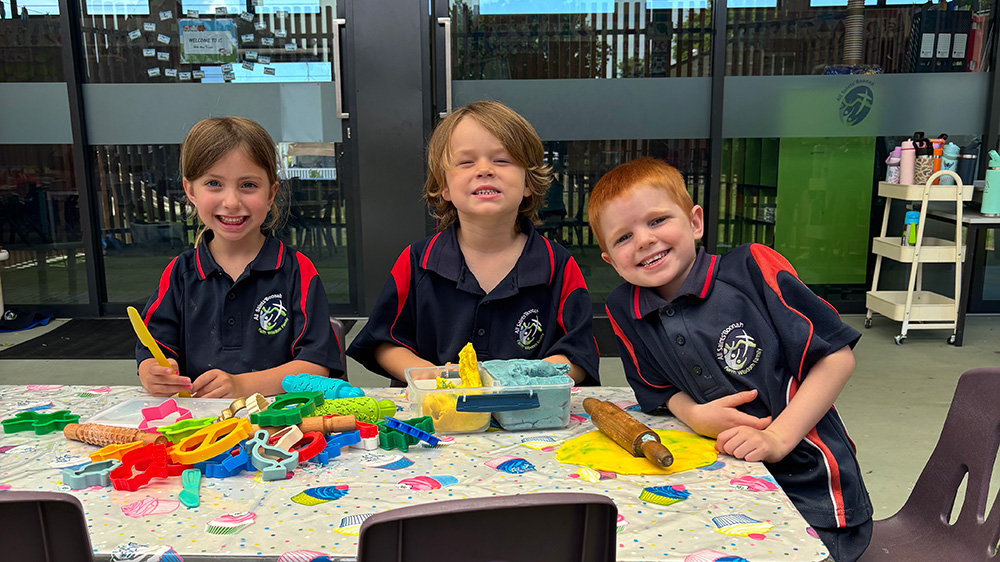 Three students sitting at a table using colourful playdough and cutters during a classroom activity